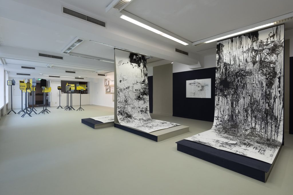 Schwarz weiß bedruckte Stoffbahnen hängen in einem weißen Raum von der Decke