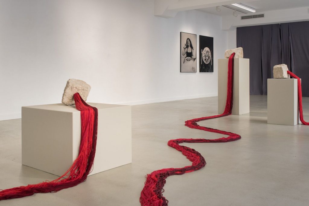 Von auf drei Säulen stehenden Skulpturen gehen rote Stoffbahnen aus