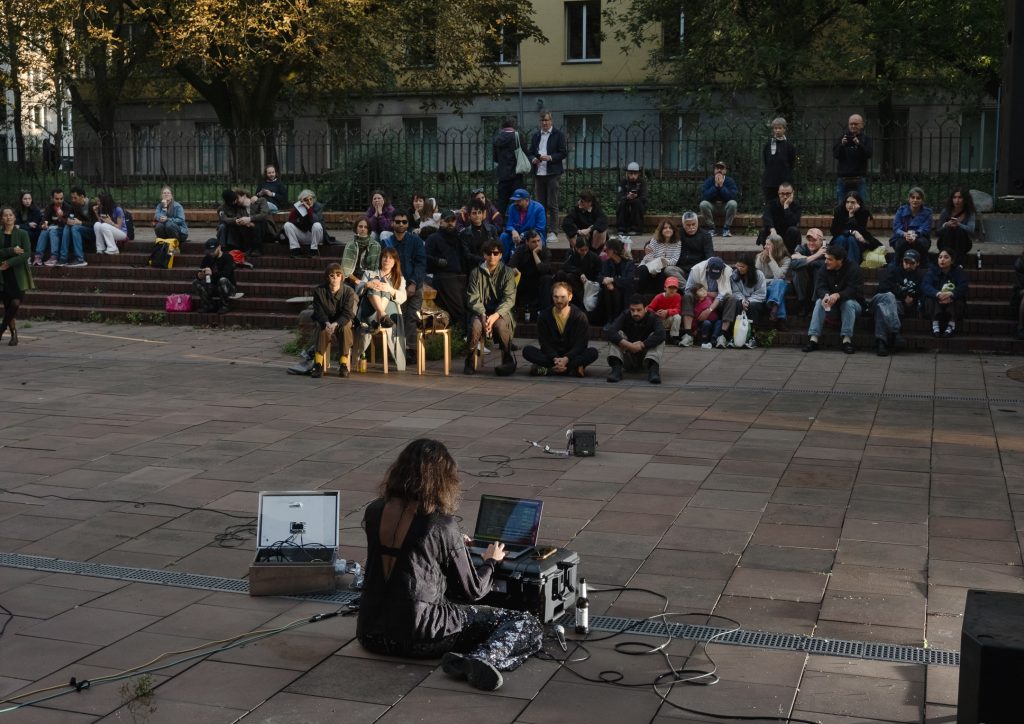 Person sitzt mit Laptop und Mikro auf dem Boden vor einem Publikum