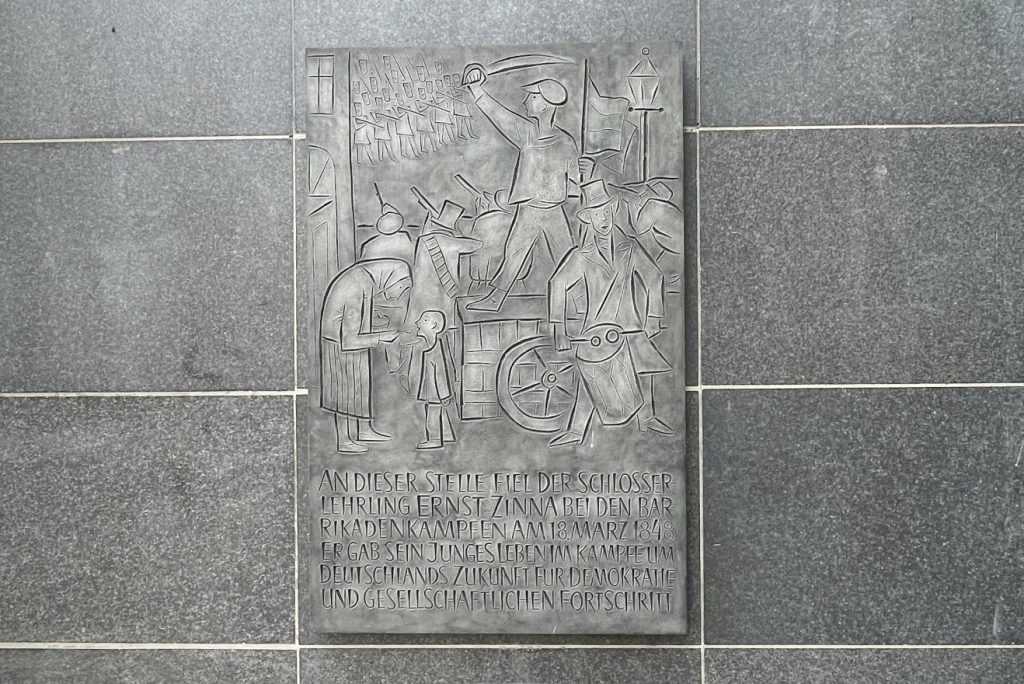 Metalltafel mit Abbildung von Barrikadenkämpfen