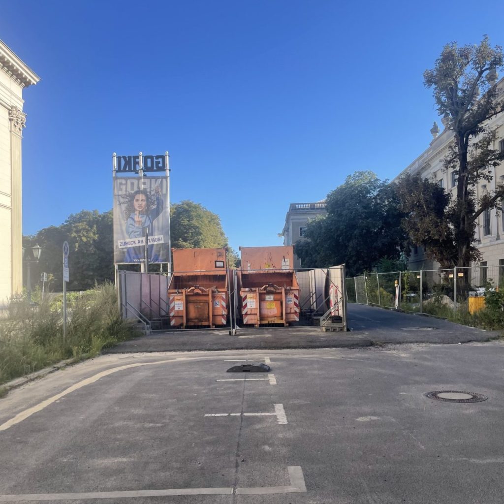 Parkplatz mit zwei Müllcontainern und Plakat des Gorki-Theaters