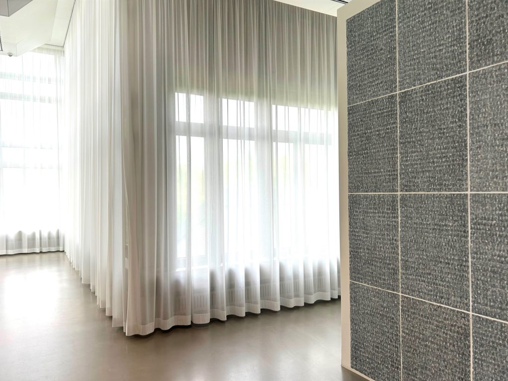 Durchsichtige Vorhänge vor Fensterfront. Licht fällt in den Raum.