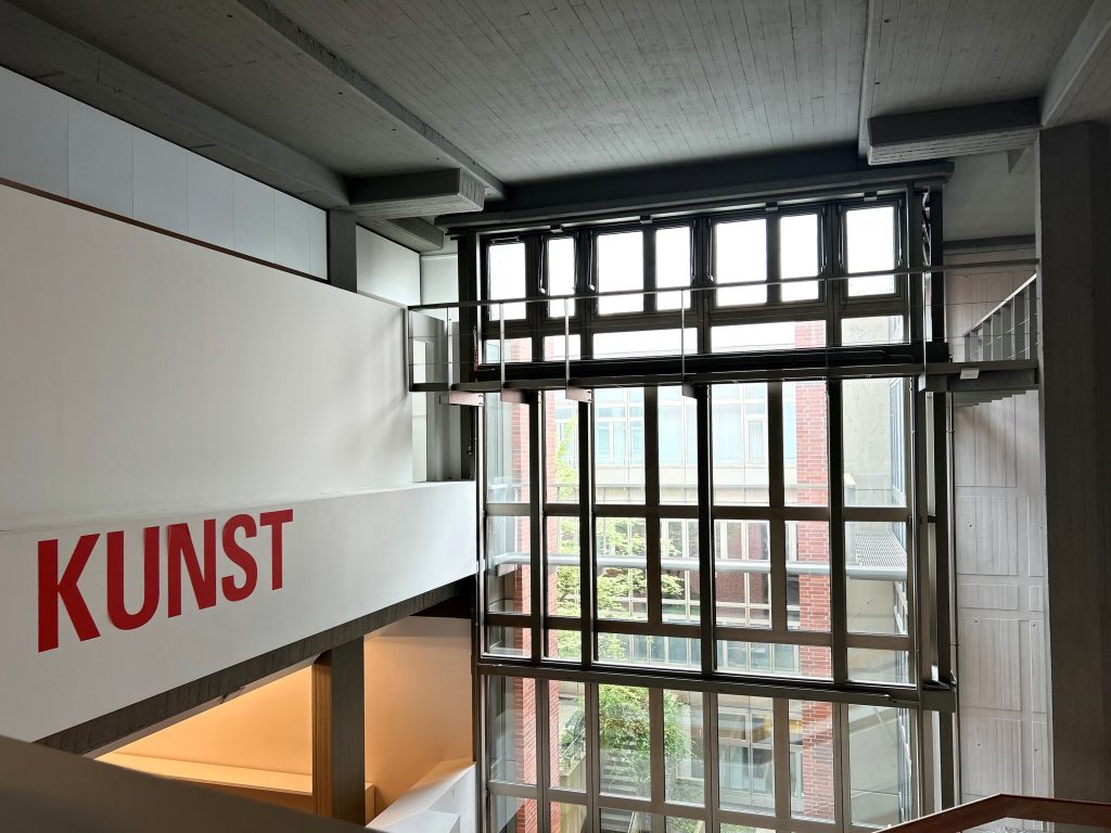 Raum mit großer Fensterfront. Auf der linken Seite weiße Wand mit roter Aufschrift