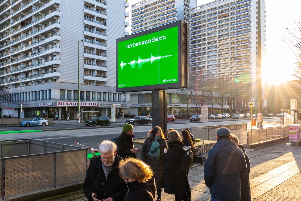 Straße in der Abendsonne mit Reklametafel mit giftgrünem Plakat, auf dem