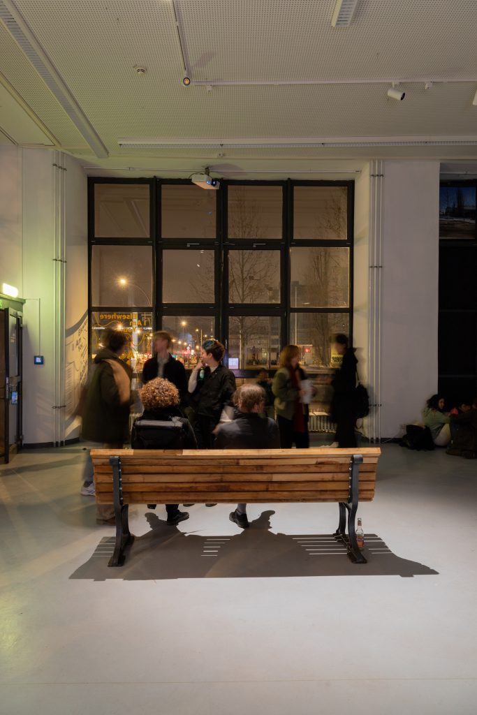 Park bench with people on it and behind it at Galerie Wedding