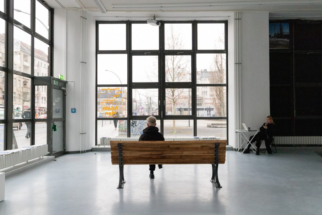 Figur auf einer Bank von hinten mit einem großen Fenster davor