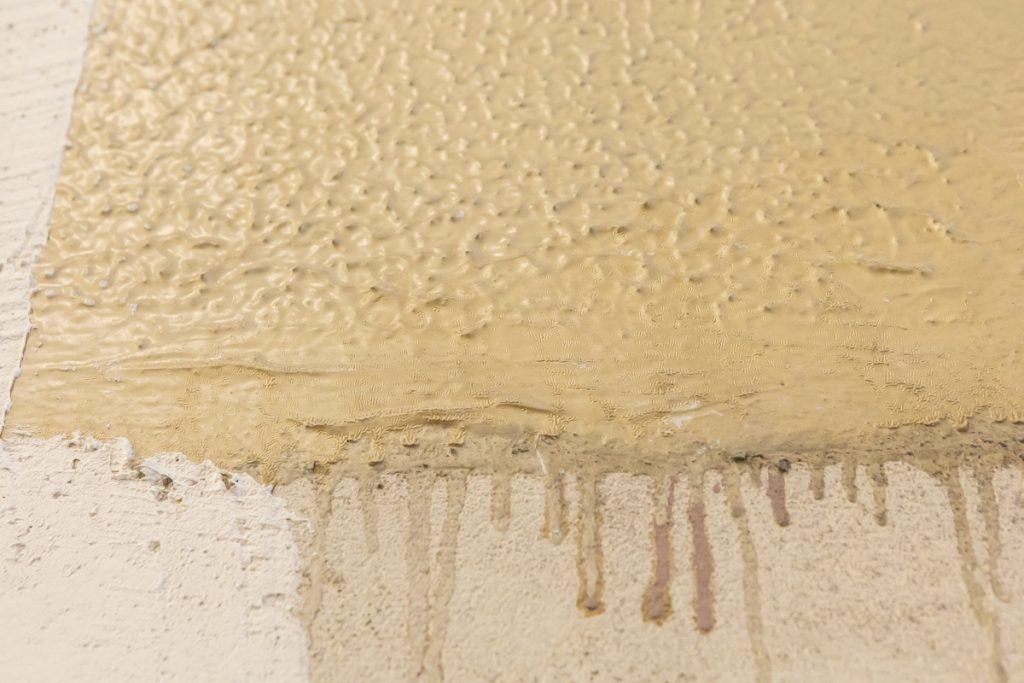 In Ocker bemalte Wandfläche mit herunterlaufender Farbe.