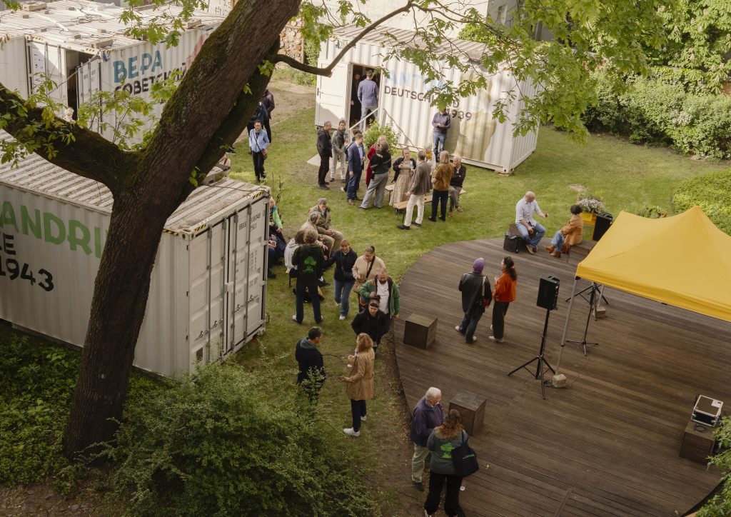 Menschen stehen auf der Wiese neben zwei Schiffscontainern