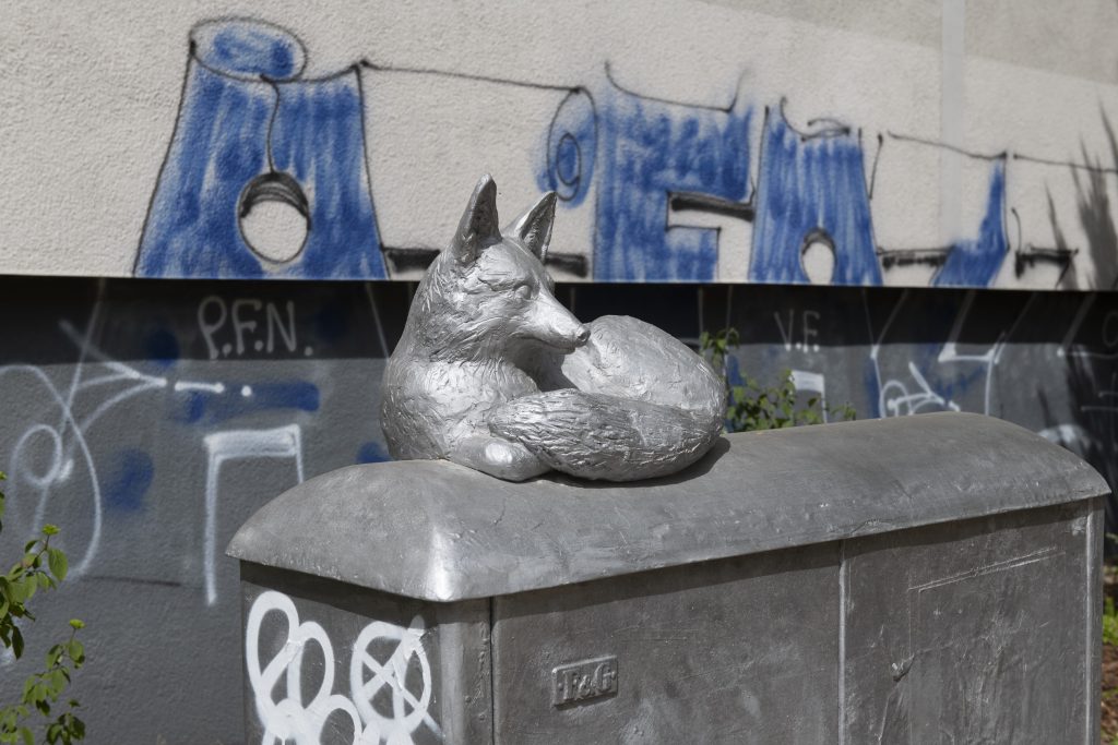 A fox made out of metal sits on an electrical box