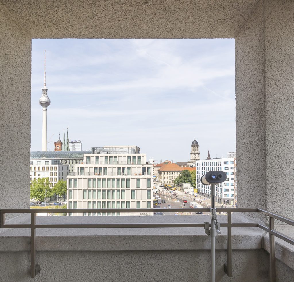 Balkon mir Fernglas an der Brüstung, blick auf die Skyline einer Stadt, die von einem Fernsehturm dominiert wird.