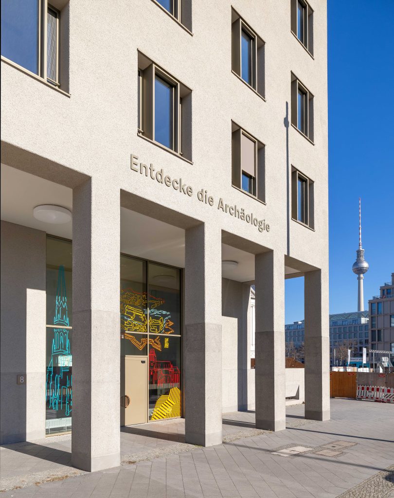 Mehrstöckiges, modernes Gebäude in grau, mit Arkadengang und Schriftzug