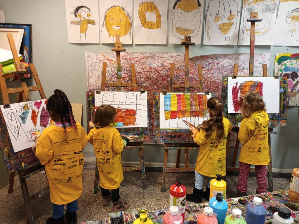 Vier Kinder in Kitteln stehen malend vor Leinwänden