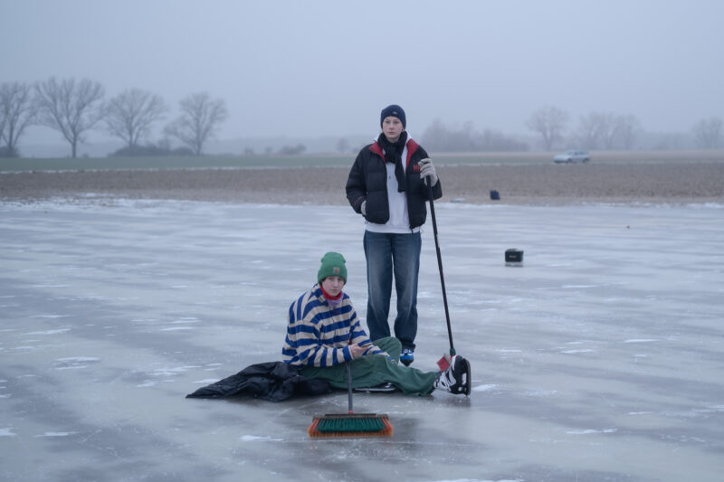 Zwei Menschen mit Besen auf einer Eisfläche, einer sitzt, einer steht