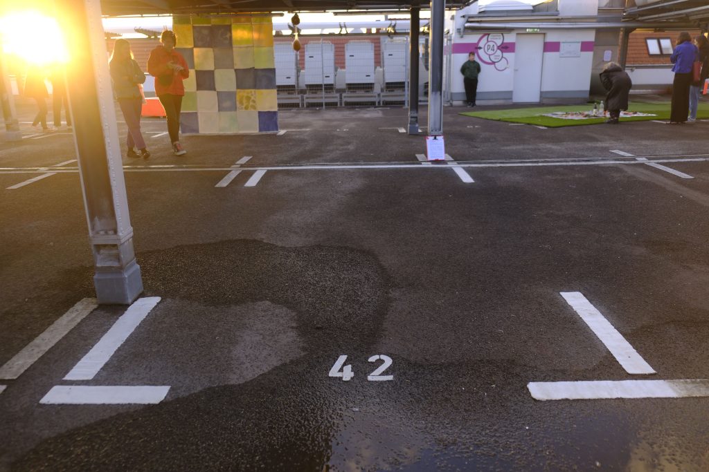 Gegenlichtaufnahme, links scheint die Sonne ins Bild, Menschen auf einem Parkdeck, rechts ist ein Picknick auf grünem Kunstrasen angerichtet.