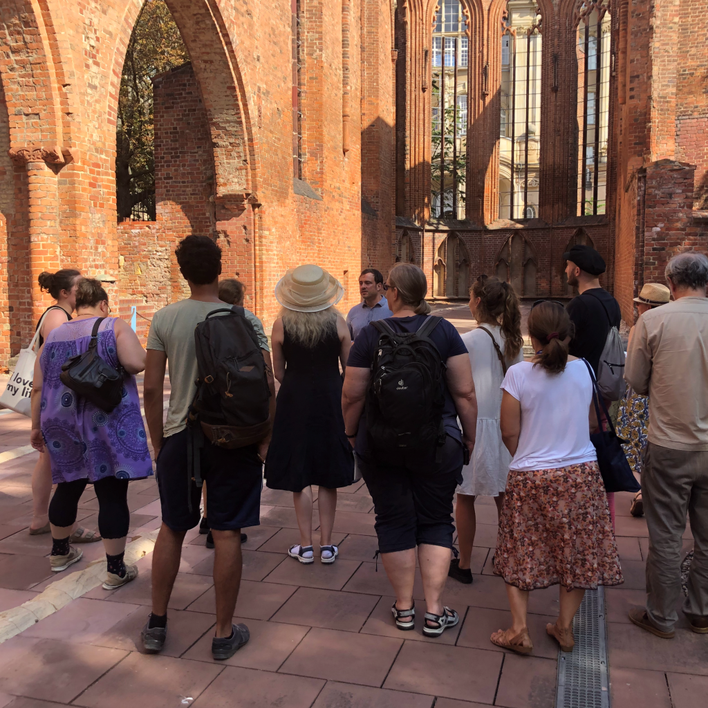 Menschen stehen mit dem Rücken zur Betrachterin vor der Klosterruine