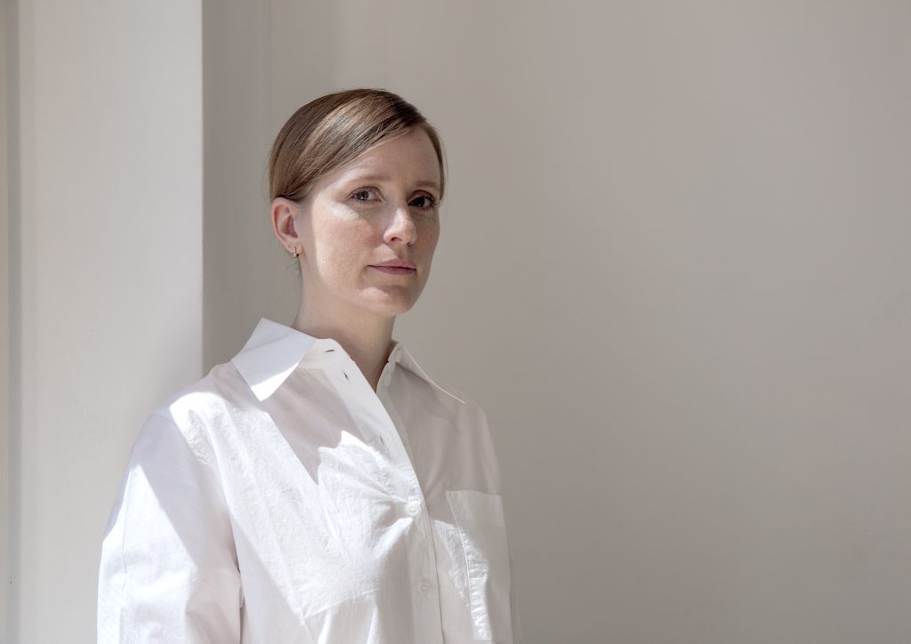 Frau im Halbprofil, weißes Hemd, vor einer weißen Wand