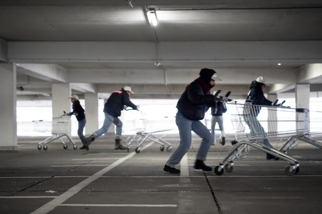 Menschen mit schwarzen Jacken schieben Einkaufswägen durch ein Parkdeck