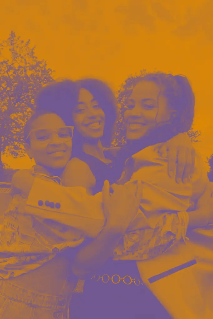 Drei junge Personen umarmen sich und lächeln in die Kamera