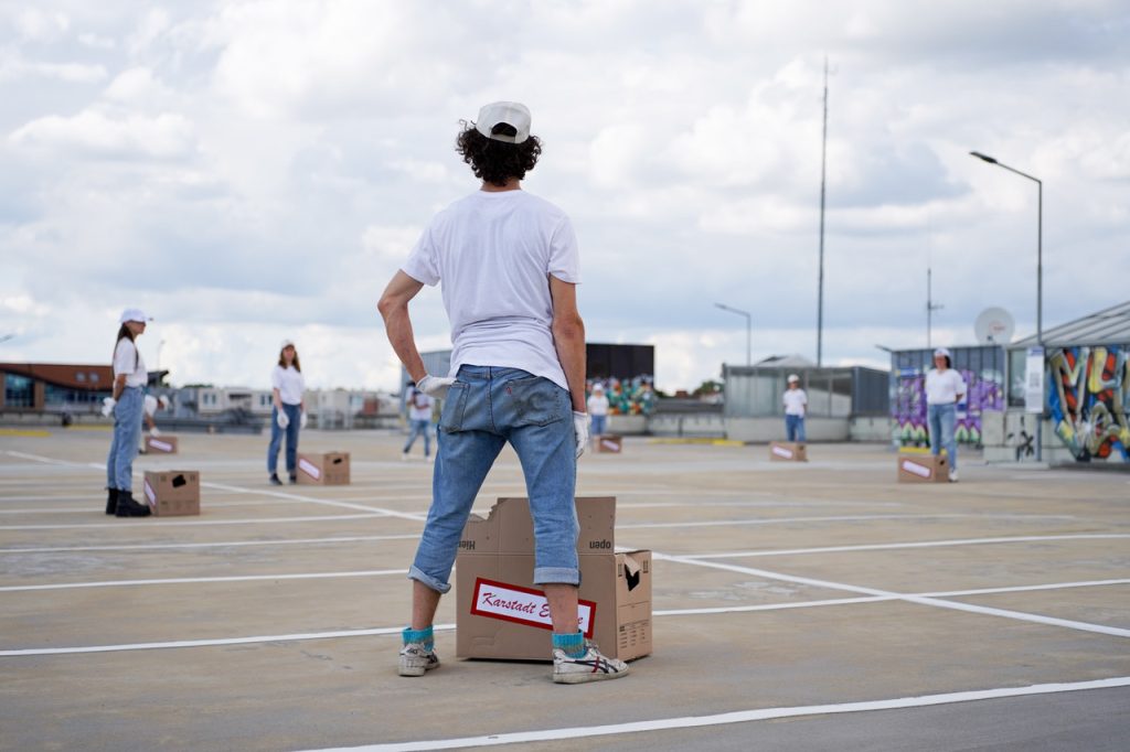 Menschen in weißen Shirts mit Pappkartons vor sich stehen auf einem Parkhausdach