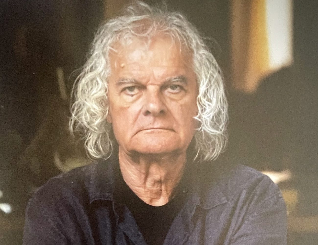 Mann mit schulterlangen grauen Haaren blickt in die Kamera